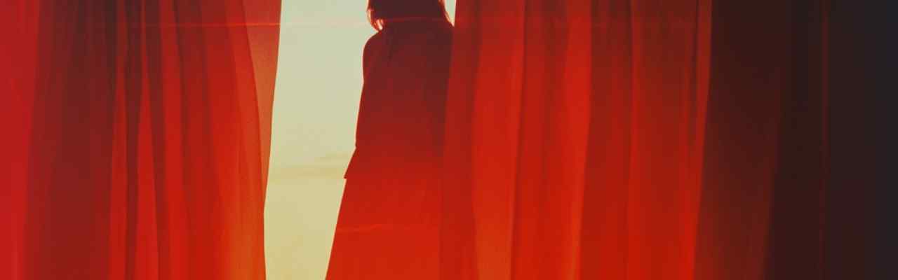 Woman standing behind red curtains, symbolizing toxic feminism vs toxic femininity in solitude