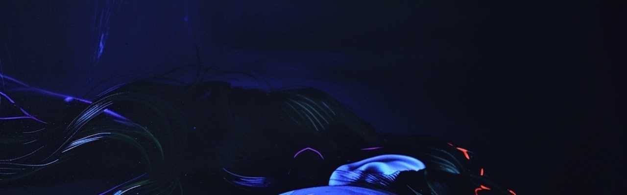 Dark, moody setting with subtle blue glow on a woman's face, evoking curiosity and romantic attraction.